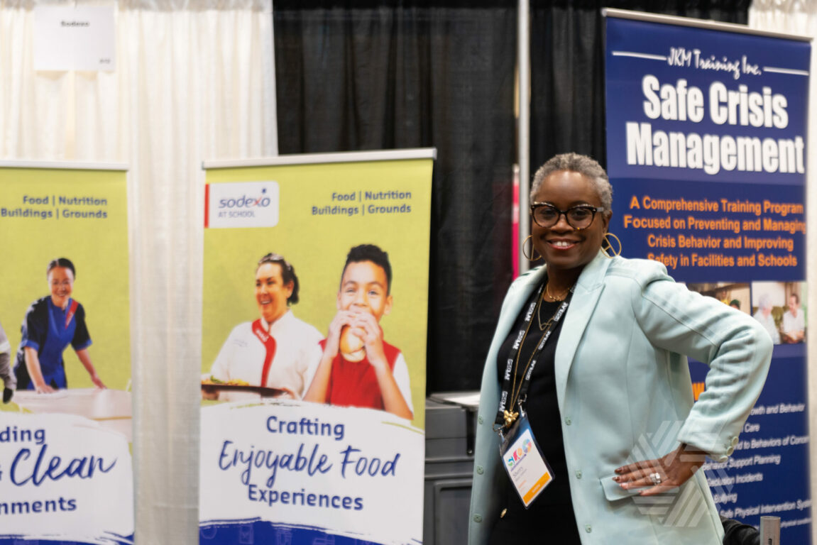 Exhibitor smiling at camera in front of booth at school leadership conference